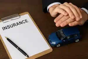 seguro-auto-2025 Carro em miniatura azul sendo protegido por mãos sobre documento de seguro