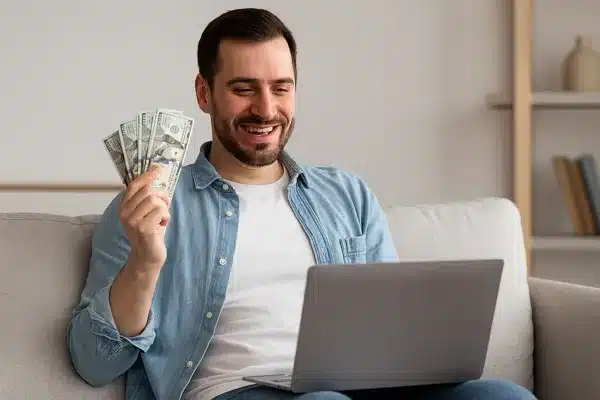 renda-extra-online-em-2025Homem feliz usando notebook e recebendo dinheiro com renda extra em 2025