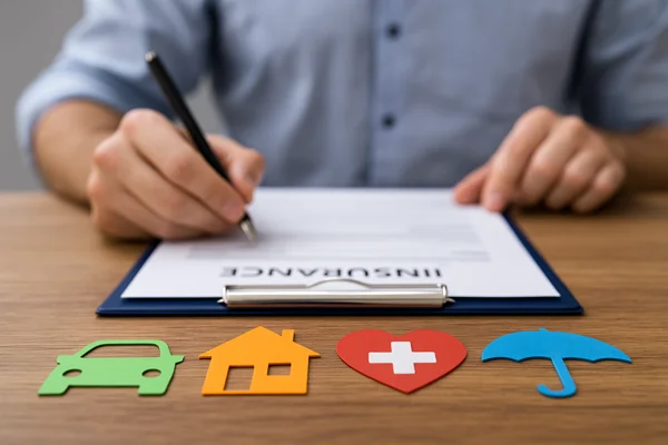 seguro-residencial-em-2025Pessoa preenchendo formulário de seguro em mesa de madeira com ícones coloridos de carro, casa, saúde e proteção