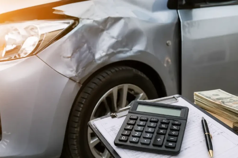 uanto Uma Batida Leve Pode Custar em 2026 com carro batido na lateral esquerda, prancheta com calculadora e caneta, dinheiro e moedas ao lado