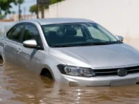 Seguro de carro cobre enchente com carro prata parcialmente submerso em rua alagada.